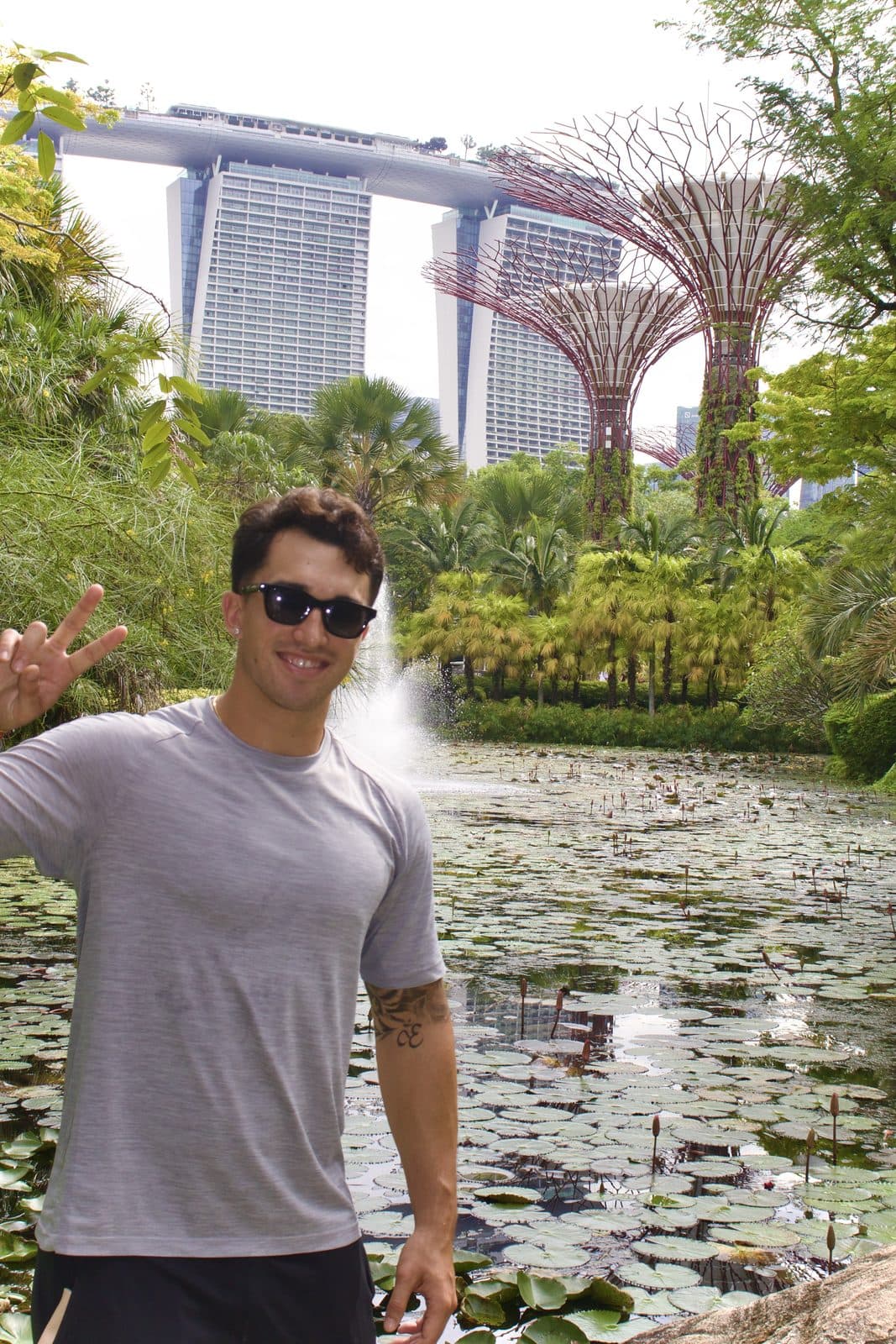 Ezekiel Contreras-Forrest at Gardens by the Bay in Singapore, standing beside a lily pond with the Supertree Grove and Marina Bay Sands behind him
